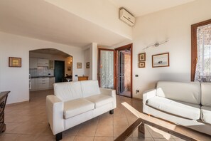 A living room with two white sofas, a kitchen in the background, and a door leading to another room. - Holiday Home "Il Pashà" near the Beach with Sea View & Garden (vilaputzu)