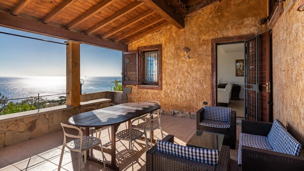 A covered outdoor seating area with a table and chairs, a wicker sofa, and a view of the sea.
