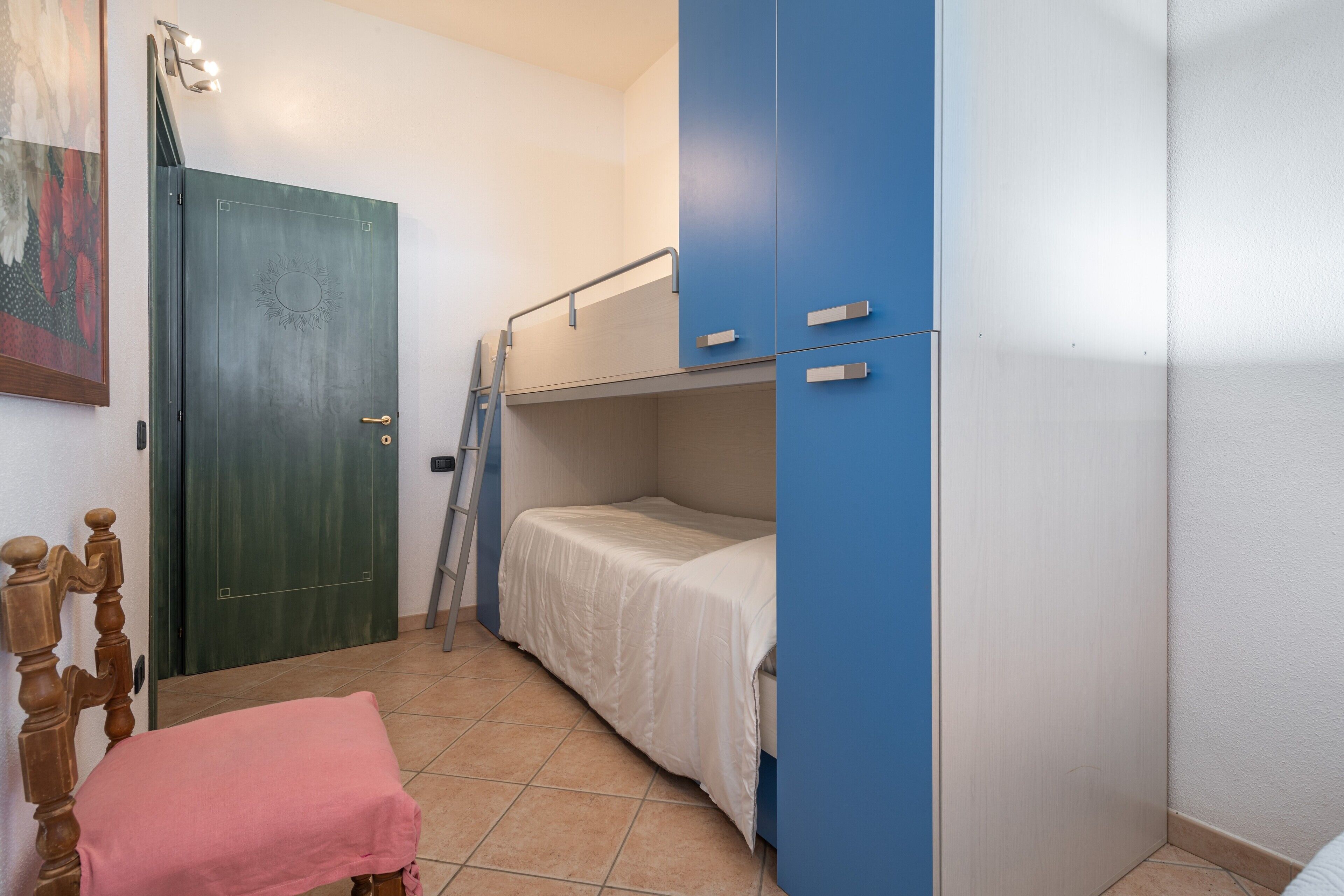 A room with a bunk bed, a wooden chair, a door, and a ladder.
