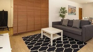 Un salon moderne avec un canapé, une table basse et un tapis à motifs. Un tableau orne le mur et une fenêtre offre une vue agréable.