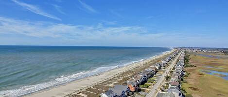 A coastal residential area with houses along the beach, a clear sky, and a road running parallel to the shore.