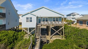 A coastal house with a wooden deck and a staircase leading to a balcony. - "Close Call" - Oceanfront Home, 4 Bedrooms / 3 Bathrooms (Holden Beach)
