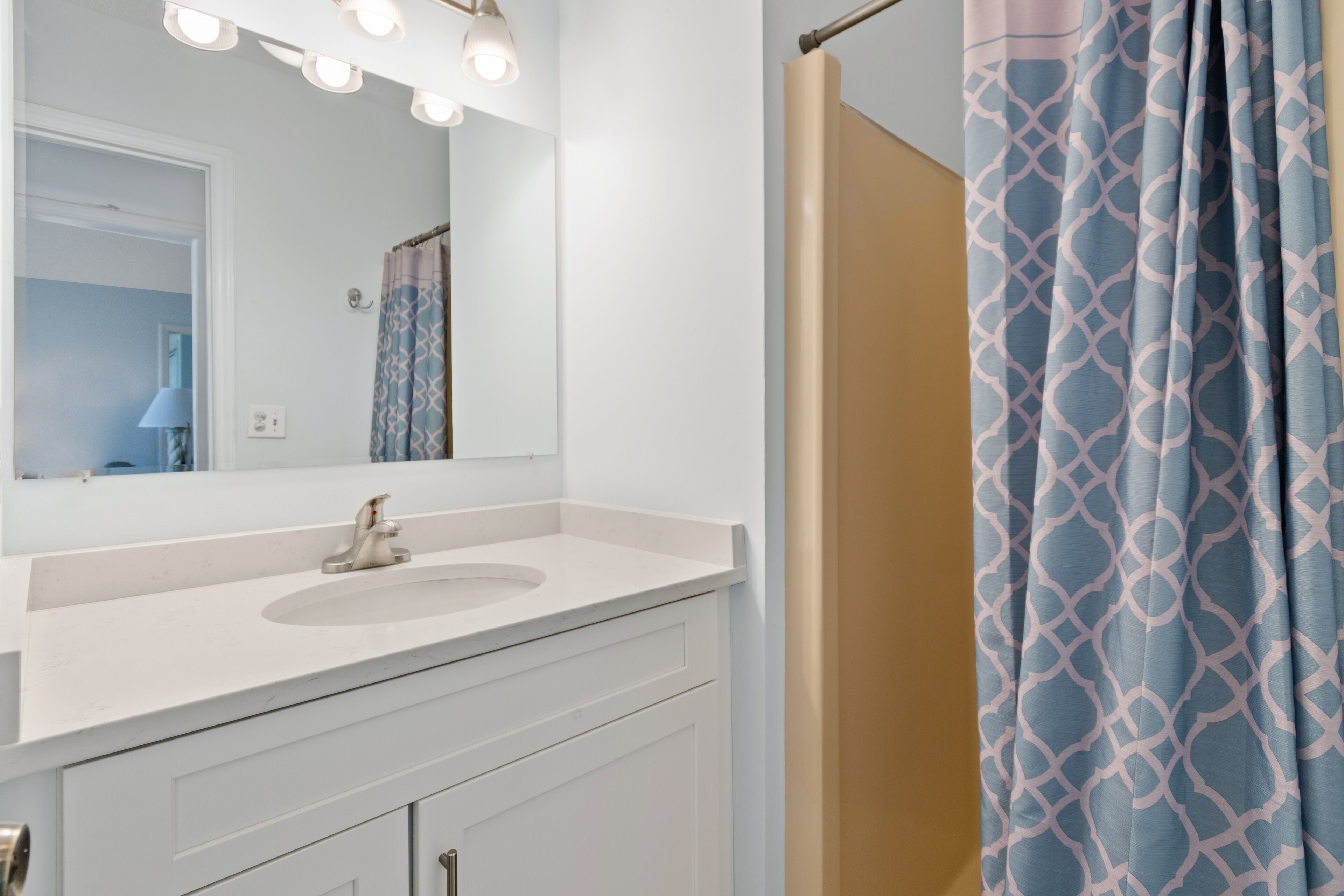 A bathroom with a white vanity, a mirror with lights, and a shower curtain with a geometric pattern.