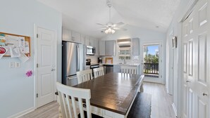 A modern kitchen with white cabinets, stainless steel appliances, and a wooden dining table. - "Close Call" - Oceanfront Home, 4 Bedrooms / 3 Bathrooms (Holden Beach)
