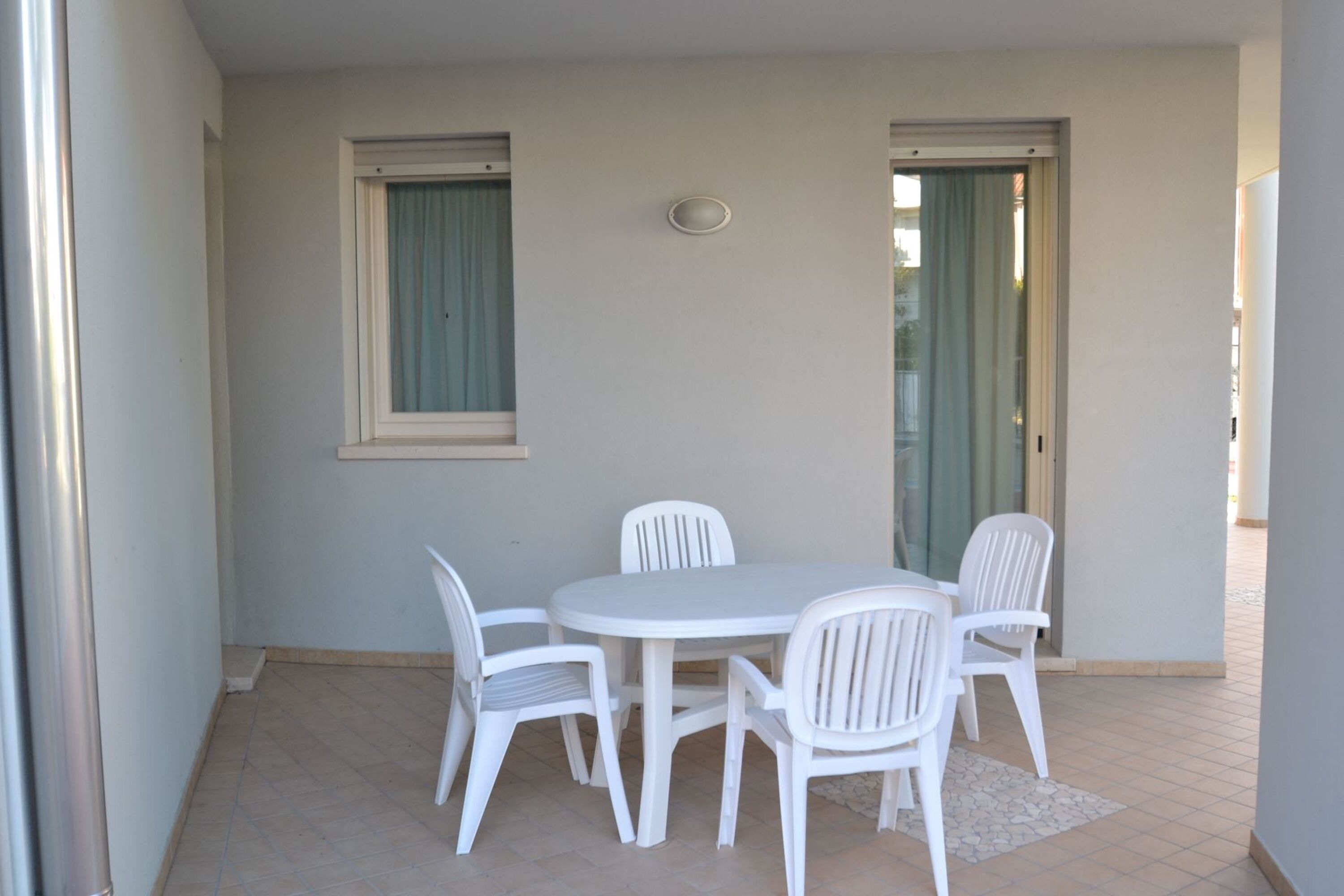 A small, enclosed outdoor dining area with a round table and four white chairs.