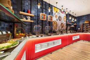 Zona de bufé con un mostrador rojo, diversas opciones de comida y decoración mural.