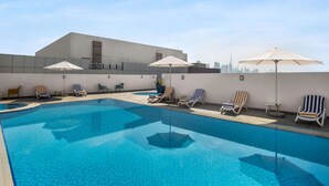 A rooftop swimming pool with lounge chairs and umbrellas, a city skyline in the background, and a modern building facade. - La Quinta by Wyndham Dubai Jumeirah (Dubai)