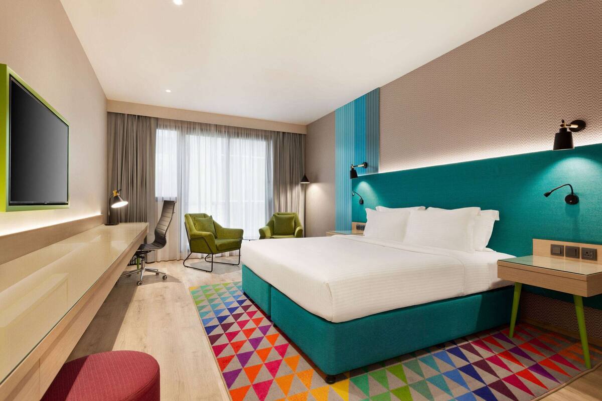 Una habitación de hotel moderna con una cama grande, dos sillas, un escritorio y un televisor.