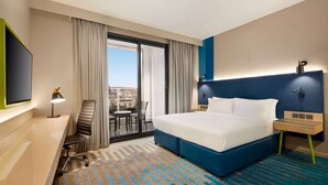 A hotel room with a large bed, a desk, a chair, a TV, and a view of the city through the window. - La Quinta by Wyndham Dubai Jumeirah (Dubai)
