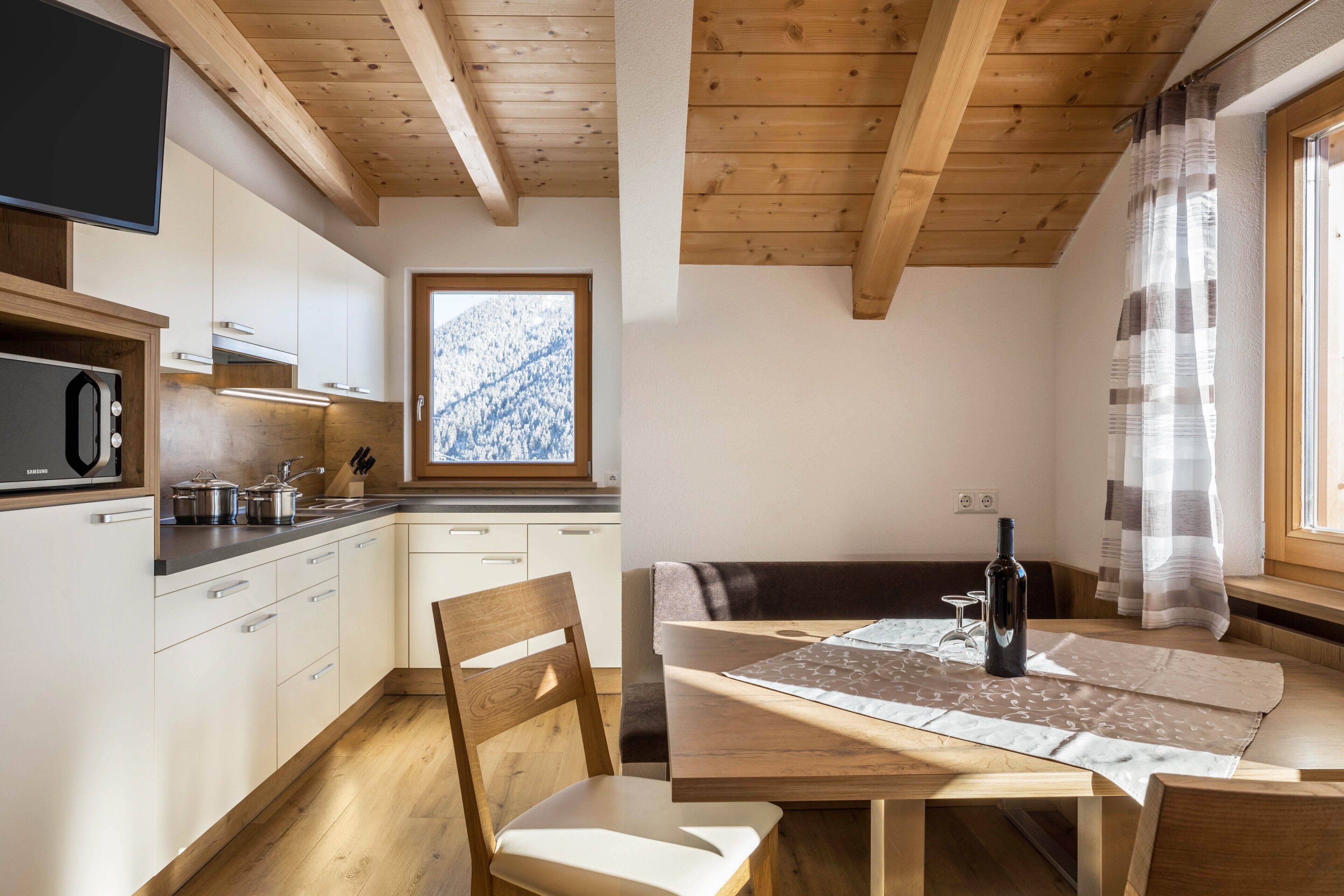 A modern kitchen with wooden beams, a dining area with a table and chairs, and a window with a mountain view.