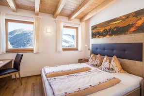 Una camera da letto con un letto, una scrivania, una sedia e due finestre vista montagna.