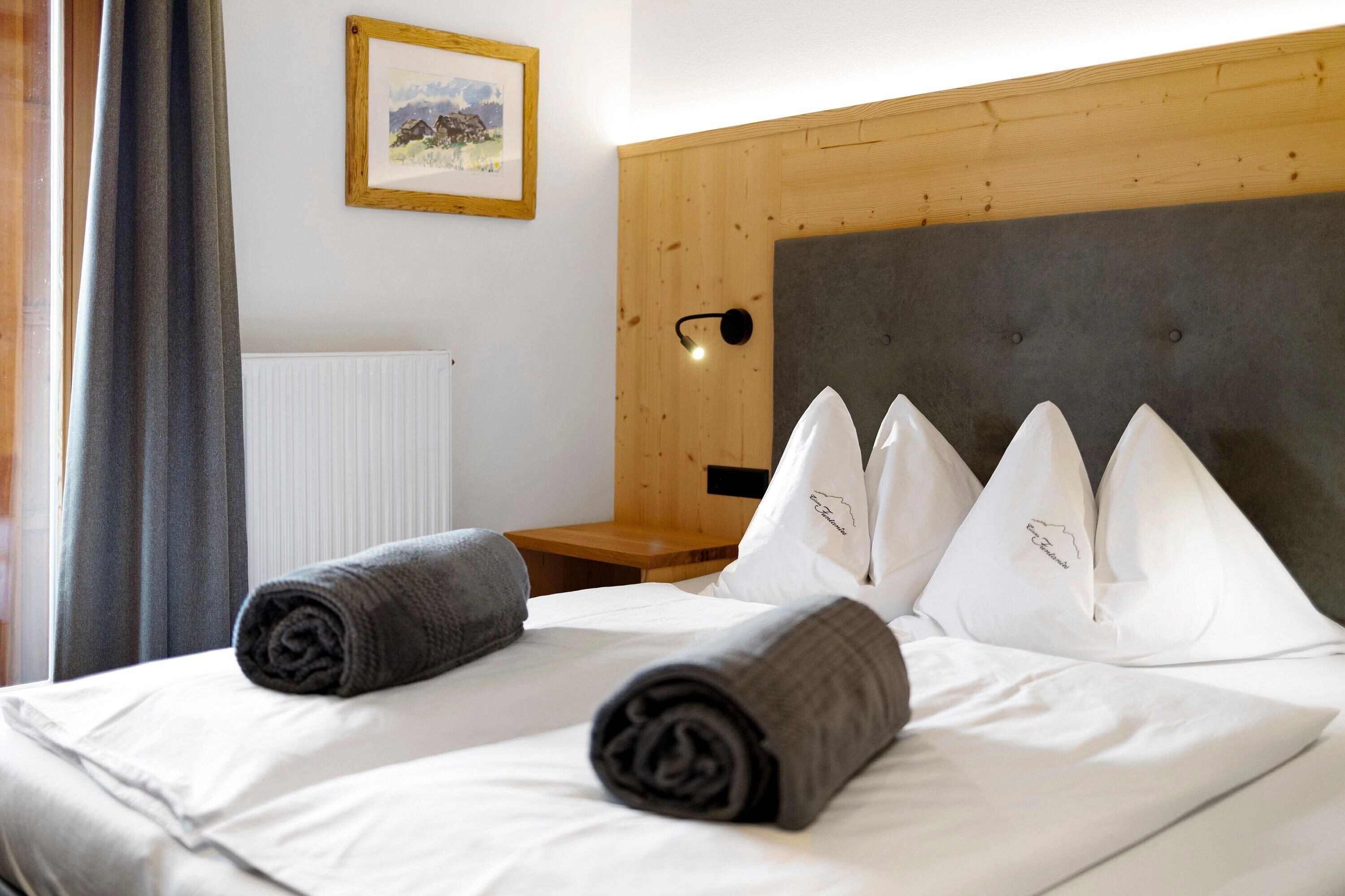 A neatly made bed with rolled towels, a framed picture on the wall, and a wooden headboard.