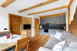 A modern kitchen with grey cabinets, a wooden dining table with chairs, and a grey sofa.