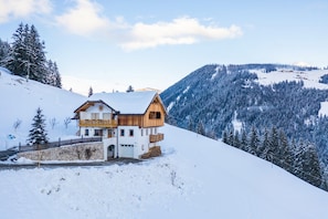A chalet with a wooden exterior, a balcony, and a stone wall.