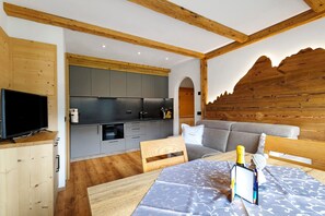 A modern kitchen with grey cabinets, wooden beams, a dining area with a table, and a sofa.