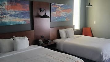 Una habitación de hotel con dos camas, una mesita de noche, una lámpara de pared y pinturas abstractas.