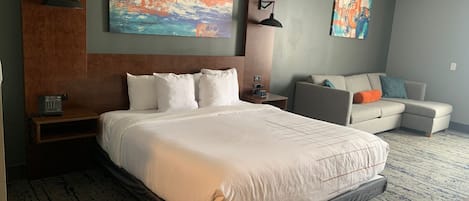 A hotel room with a large bed, a sofa, and two abstract paintings on the wall.