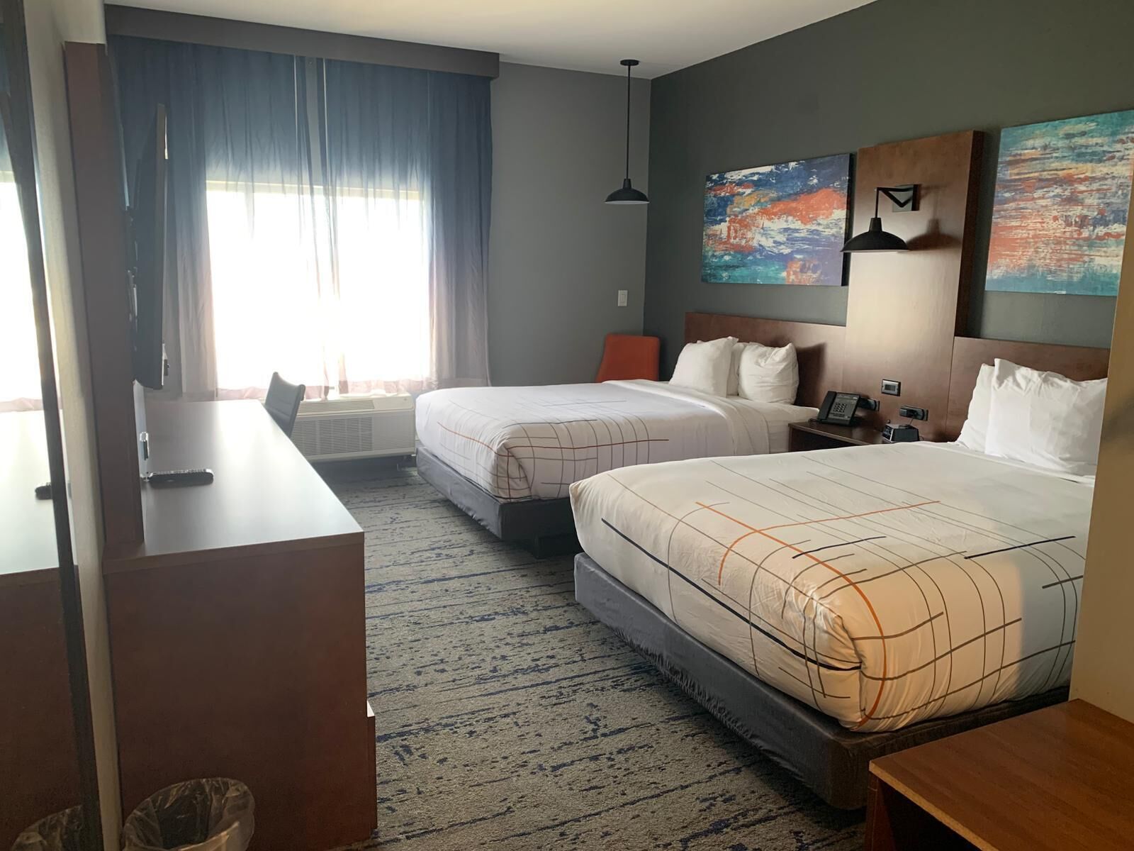 A hotel room with two beds, a desk, a chair, a desk lamp, a phone, and artwork on the walls.