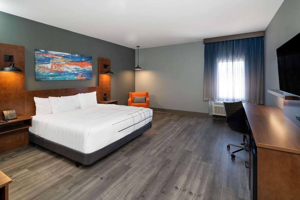 Une chambre d’hôtel avec un grand lit, un bureau, une chaise, une télévision et un tableau au mur.