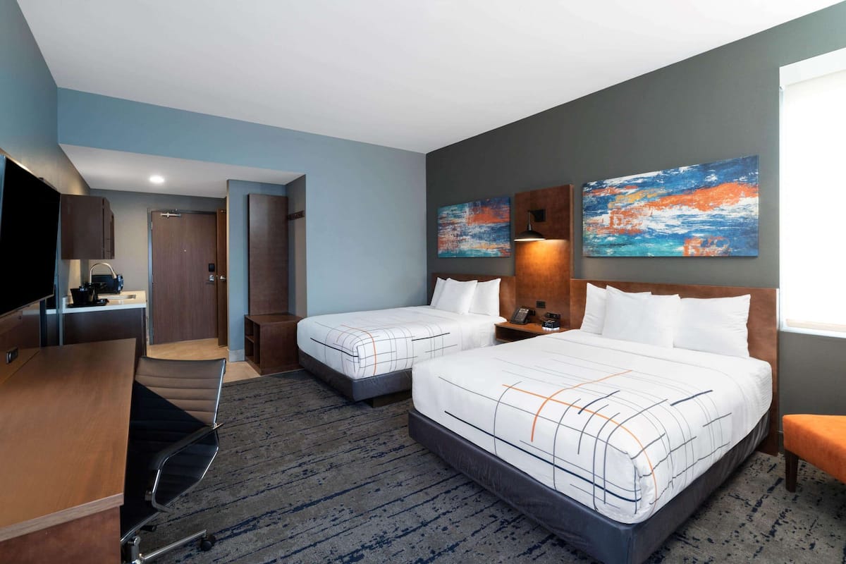 Une chambre d’hôtel avec deux lits, un bureau, une chaise, une télévision et des œuvres d’art accrochées aux murs.