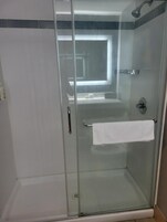 Ducha con cerramiento de vidrio, toallero blanco y cabezal de ducha visible.