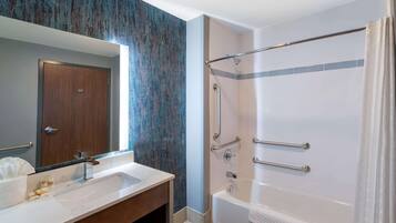 A modern bathroom with a large mirror, a white sink, and a walk-in shower with grab bars.