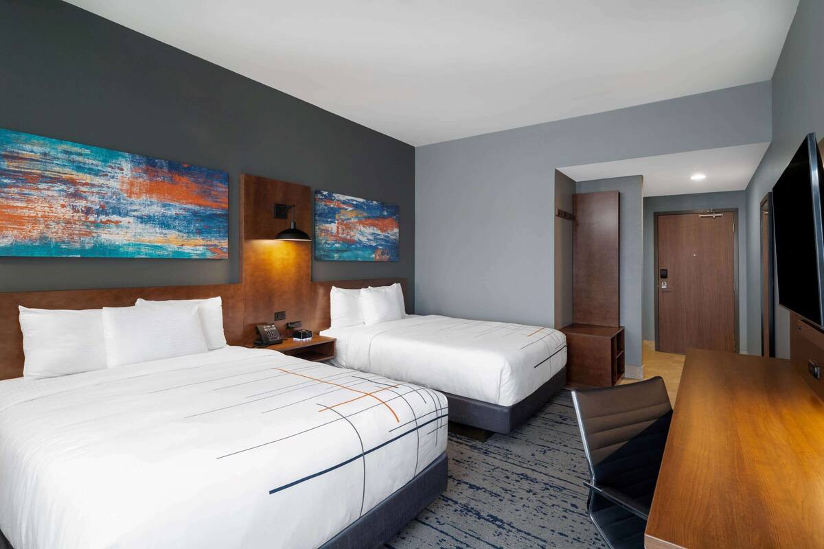 Une chambre d’hôtel avec deux lits, un bureau, une chaise, une télévision et des œuvres d’art accrochées aux murs.