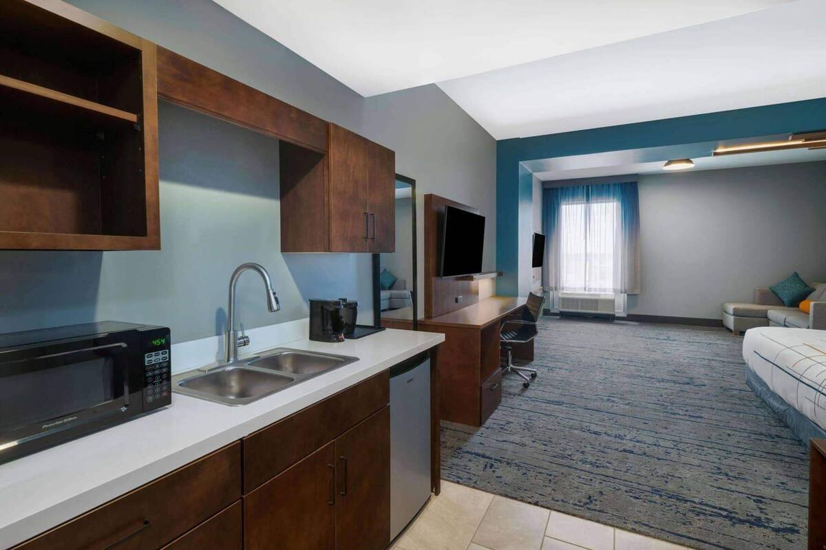 Une chambre d’hôtel moderne dotée d’une kitchenette, d’un coin salon et d’une grande fenêtre.