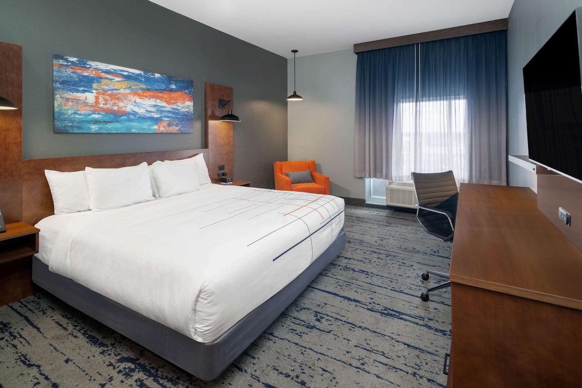 Une chambre d’hôtel avec un grand lit, un bureau, une chaise orange, une télévision et un tableau au mur.