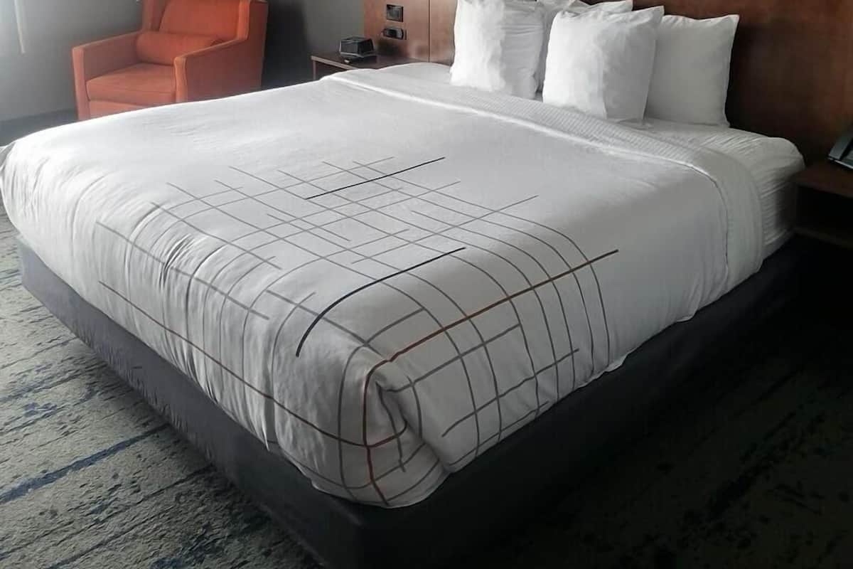 Une chambre d’hôtel avec un grand lit, une chaise, un tableau et une table de chevet.