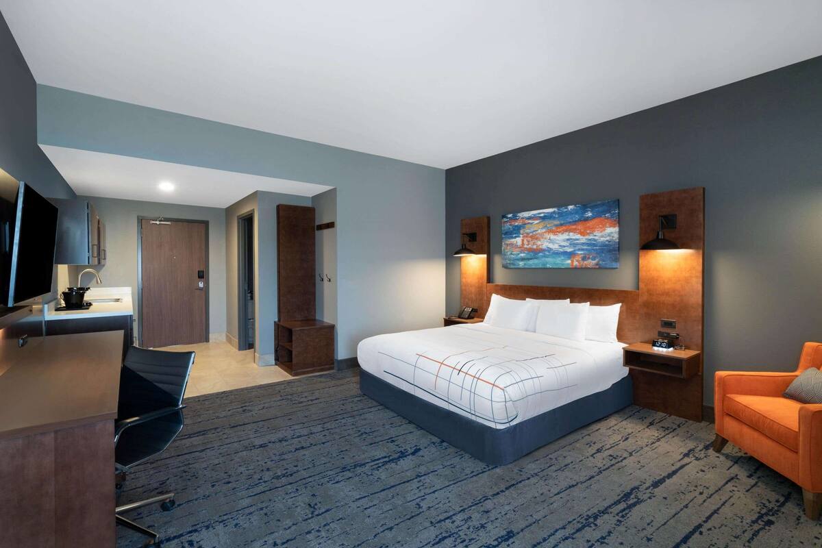 Une chambre d’hôtel moderne, dotée d’un grand lit, d’un bureau, d’une chaise, d’une télévision et d’un tableau au mur.