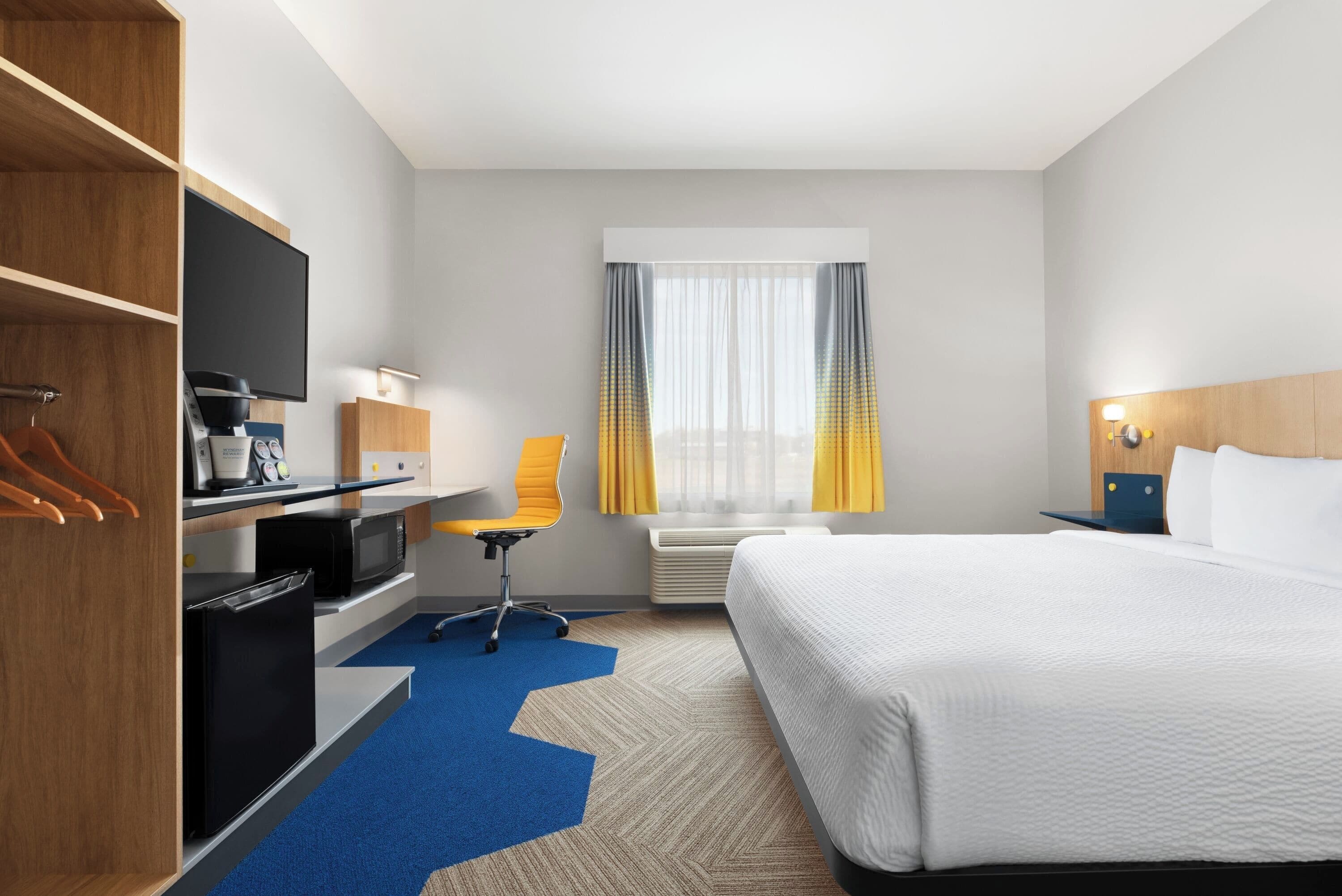 A hotel room with a bed, desk, television, and a view of the city.