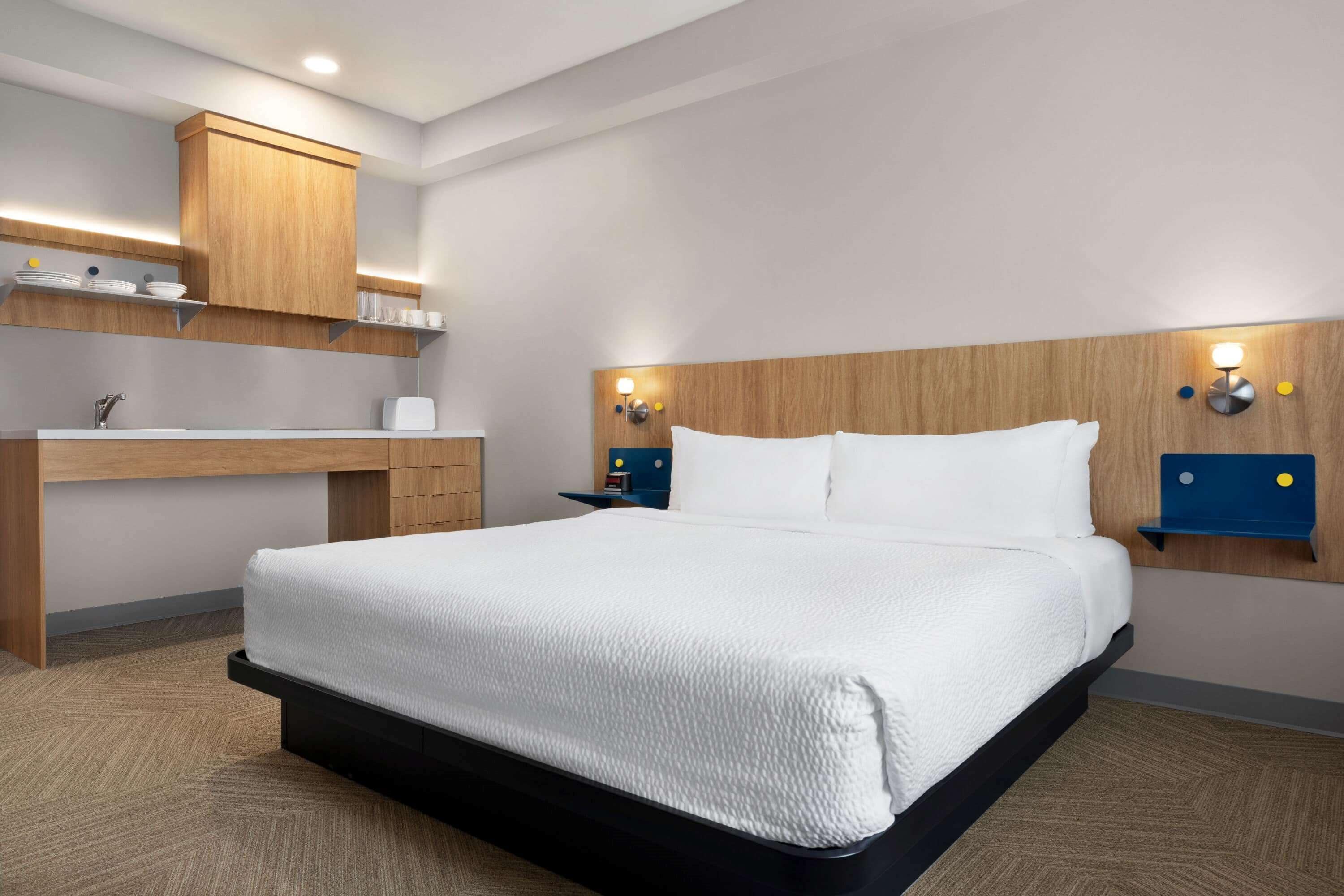 A hotel room with a bed, a desk with a sink, and a mirror.