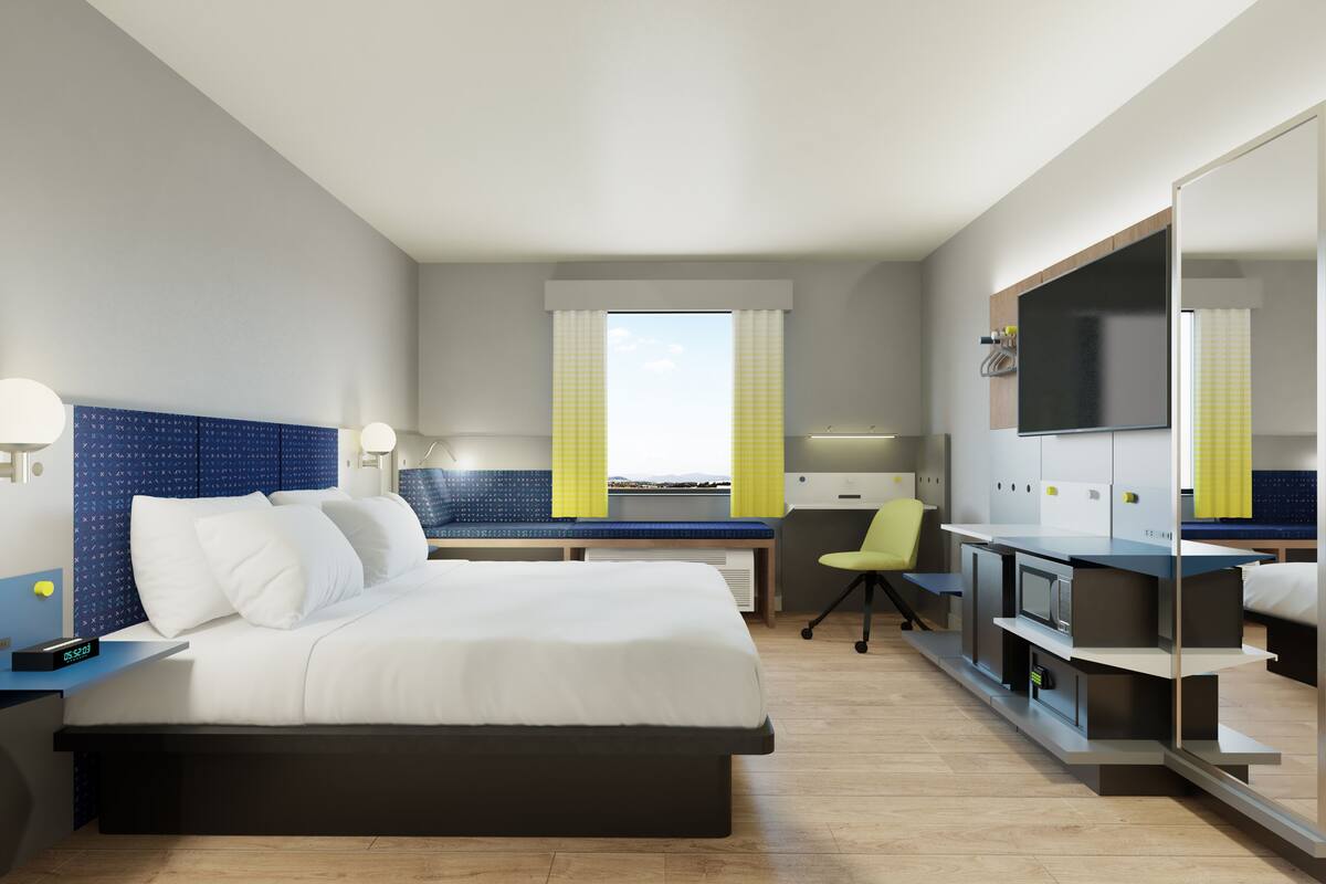 A modern hotel room with a bed, desk, chair, and a TV.