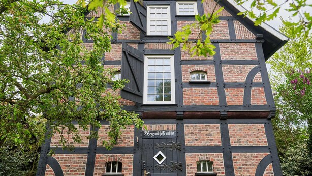 Un edificio tradicional con entramado de madera y un llamativo puerta negra, rodeado de vegetación.