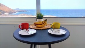Una mesa con vista al océano, una planta y un plátano sobre un mantel tejido.
