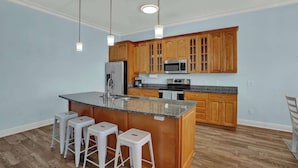 A kitchen with wooden cabinets, a granite countertop, stainless steel appliances, and white bar stools.
