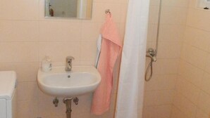 Un baño con lavamanos, espejo, ducha y una toalla rosa colgada en la pared.