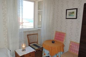 A room with a bed, a chair, a small table with a lamp, and a window with a view of the beach. - Villa Hortenzia (Dubrovnik)