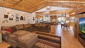 Interior acogedor de una cabaña con un amplio techo de madera, un sofá modular, un comedor y una cocina.