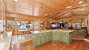 Een ruim houten blokhutinterieur met een groot kookeiland, een eethoek en een gezellige woonkamer met open haard.