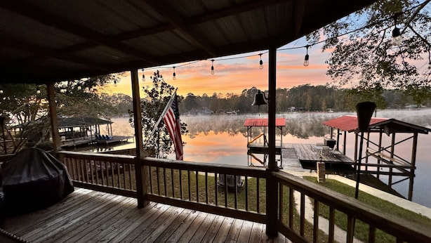 A wooden deck with a view of a lake, a gazebo, and a dock.