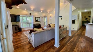 A spacious living area with a large gray sofa, wooden flooring, a mounted deer head, and a television.