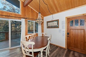 Un coin repas avec une table ronde en bois et des chaises blanches, un lustre et une porte en bois dotée de panneaux de verre.