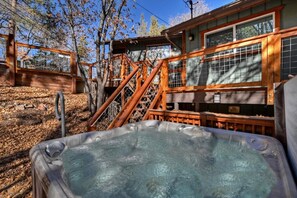 A hot tub in a natural setting with wooden deck and stone walls. - Birdsong Cabin by Destination Big Bear : Luxury! Walk to Bear Mountain Resort! Outdoor Hot Tub! Pac Man Arcade! (Big Bear Lake)