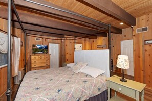 Een slaapkamer met een hemelbed, houten wanden, een dressoir, een televisie en een lamp.