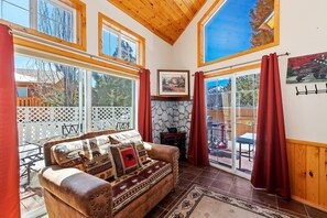 A cozy living room with a leather sofa, a stone fireplace, and large windows.