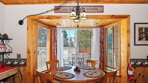 A wooden interior with a dining table, chairs, a chandelier, and a sign reading 'WELCOME THE WOODS.' - Nestled in the Upper Moonridge with Beautiful Views! Outdoor Hot Tub in Fenced Yard! Game Room! Two Master Suites! (Big Bear City)