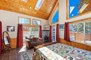 A room with a large bed, a wooden ceiling, and multiple windows.