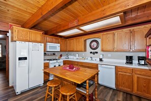 Una cocina con armarios de madera, microondas, estufa y una mesa con taburetes.